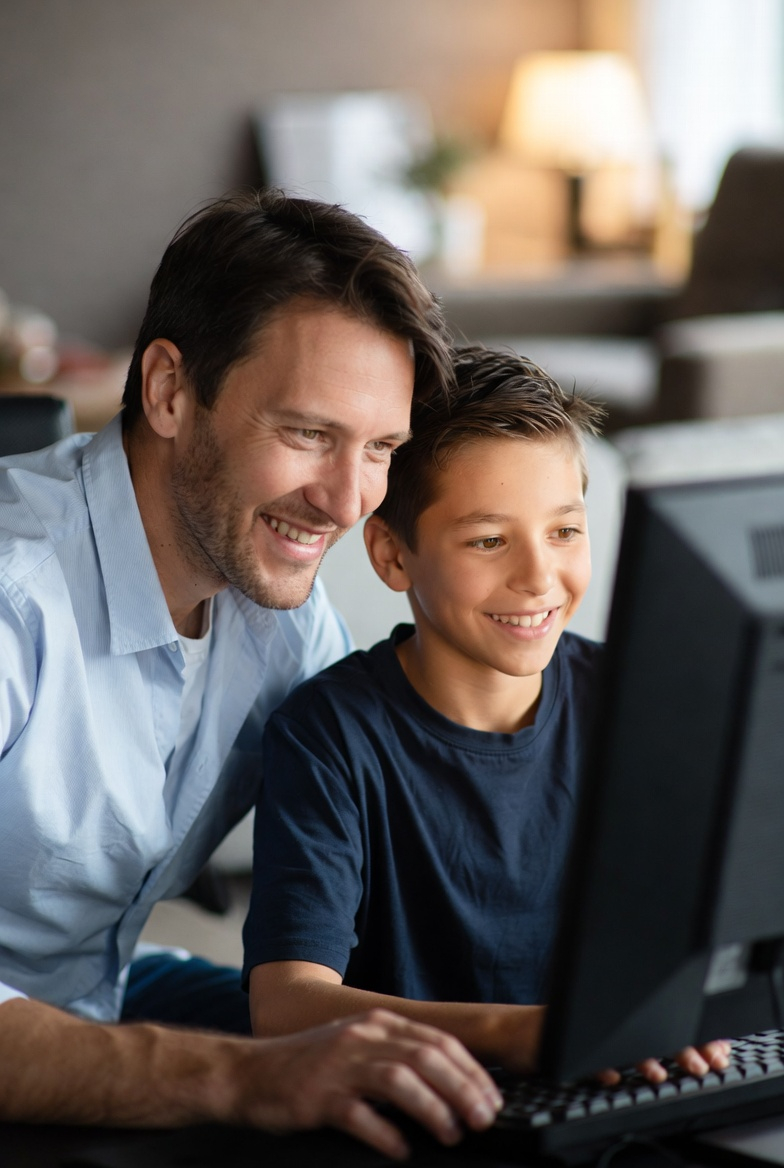 Vater sitzt neben dem Sohn, beide schauen auf einen Desktop und spielen Game Detective.