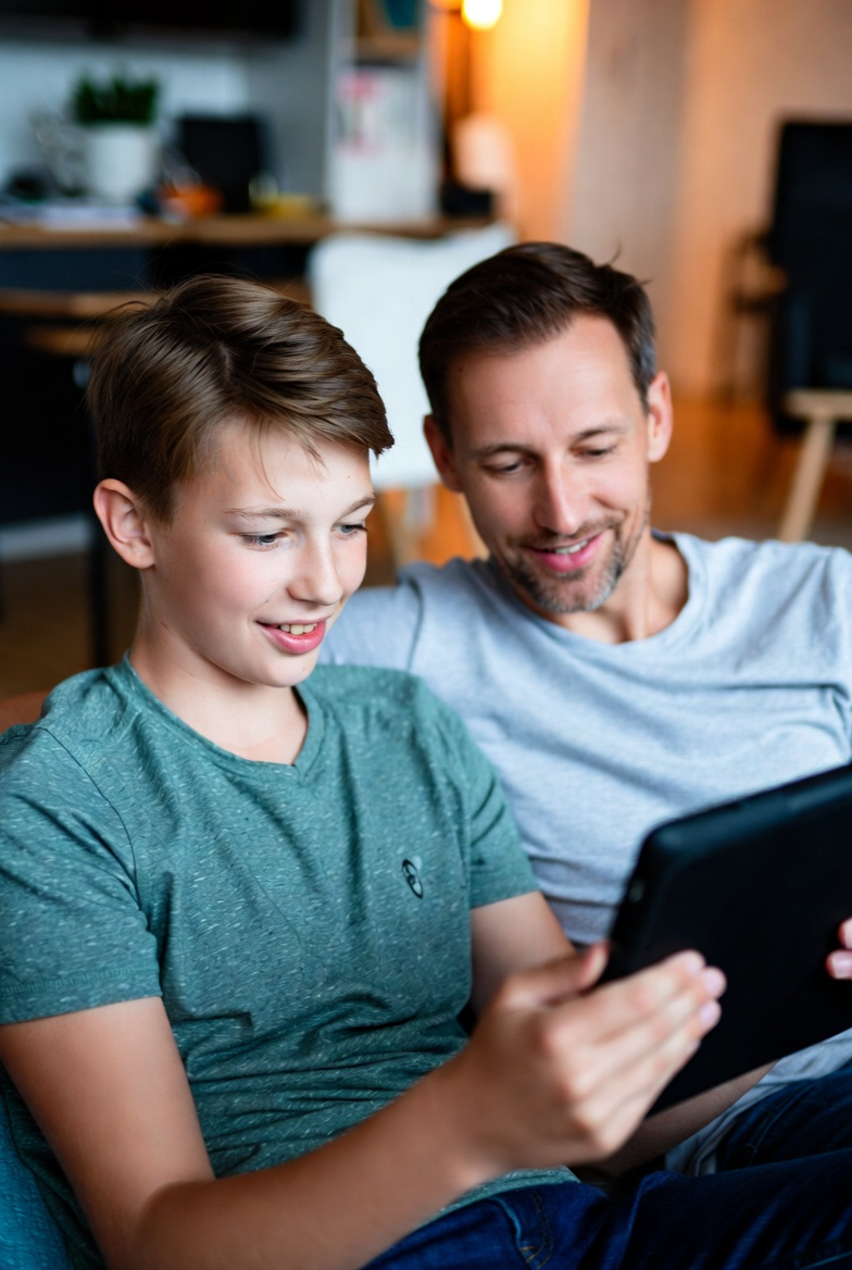 Vater und Sohn sitzen auf der Couch mit dem Tablet spielen gemeinsam Strategy Mission