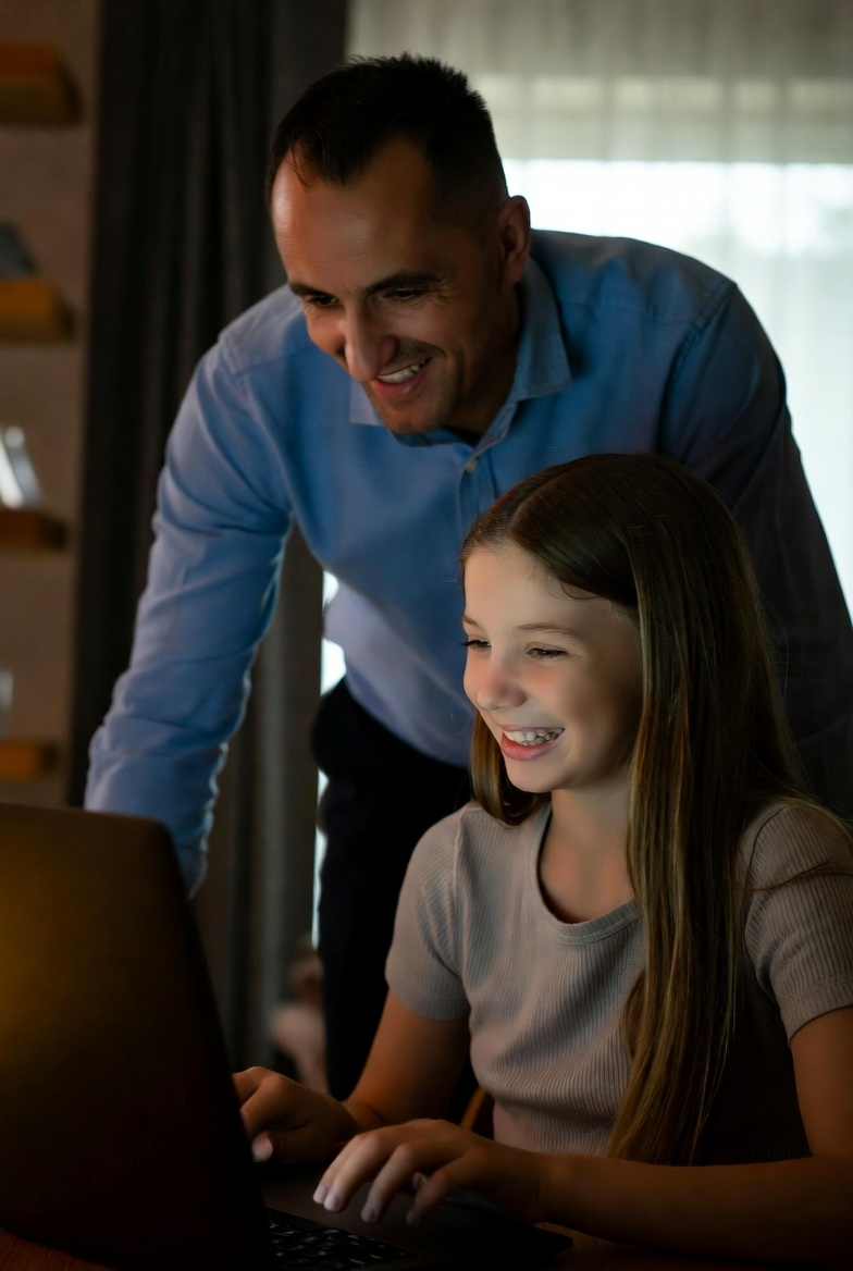 Vater steht hinter der Tochter und schaut ihr zu während sie ihm die TutorPlai Spiele zeigt.